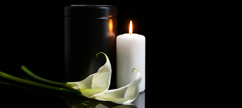 um lírio, uma vela e uma urna com cinzas da cremação